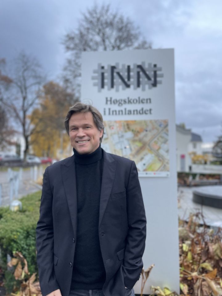 Leif Holst Jensen står utendørs foran et skilt med Høgskolen i Innlandet sin logo