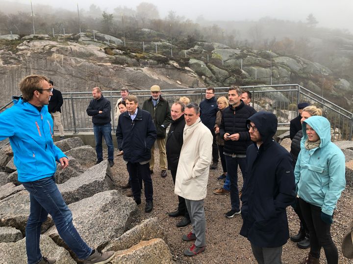 Prosjektleder Tor Åmdal forteller diplomatene  om arbeidet ved Skjerkevatn i noe surt høstvær.
