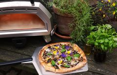 Pizza er storfavoritt på norsk middagsbord, og nå får stadig flere øynene opp for pizzaovnene til Ooni. Her pizzaovnen Karu 16, og en nystekt pizza pyntet med sommerblomster.
