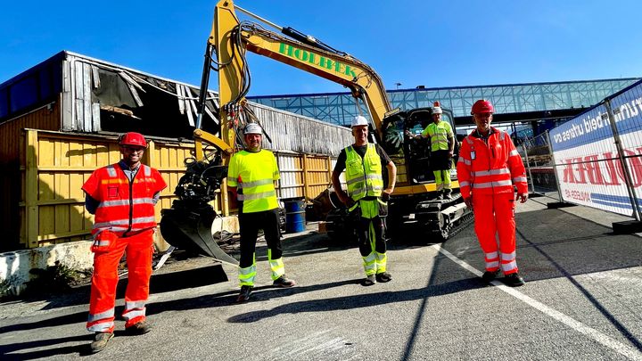 Fra venstre: Erling André Flo, byggeleder for infrastruktur i prosjektet E18/E39 Gartnerløkka-Kolsdalen i Statens vegvesen, Guttorm Andreas Høigilt, daglig leder, Øyvind Viksnes, byggeleder og Asbjørn Linde, maskinfører, alle tre i Holbæk Anlegg AS med hovedkontor i Vennesla. Helt til høyre i bildet, Nils Ragnar Tvedt i Statens vegvesen, prosjektleder for E18/E39 Gartnerløkka-Kolsdalen. Her står de alle foran den 10-tonns elektriske gravemaskinen. Foto: Statens vegvesen/Samir Kolukcija