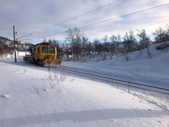 Arbeidstog kommer kjørende på jernbanespor. Skispor kan sees på tvers over jernbanesporet foran toget