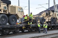 Mannskap i gule arbeidsklær fester militære kjøretøy på jernbanevogner.