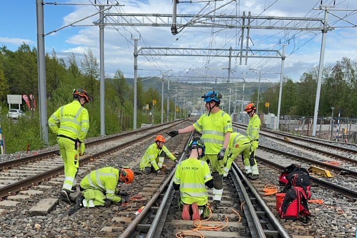 Menn i gule arbeidsklær vedlikeholder og fornyer jernbanespor.