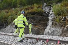Elv renner mot jernbanespor. Tre menn i gule arbeidsklær undersøker stedet.