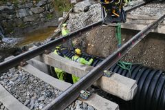 To menn i gult arbeidstøy legger stor stikkrenne under jernbaneskinner