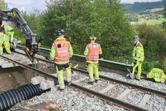 Menn i gule arbeidsklær og gravemaskin legger stort dreneringsrør under jernbanen.