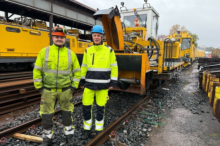 Menn i gule arbeidsklær foran skinnegående brøytemaskiner for jernbanen.