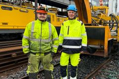 To menn i gule arbeidsklær foran gul skinnegående brøytemaskin