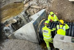 Menn i gule arbeidsklær jobber med å sette på plass en stor stikkrenne av betong under jernbanen.