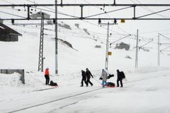 Fem personer med bagasje trekker oppakning over sporet på pulk/akebrett.