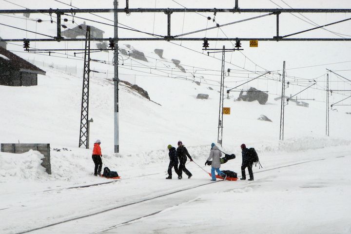 Fem personer med bagasje trekker oppakning over sporet på pulk/akebrett.