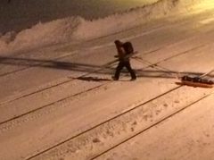En skiturist trekker en pulk over snødekt togspor.