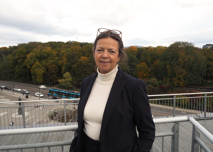 Kvinne i halvfigur ser mot kamera. Trafikk og skog i bakgrunnen.