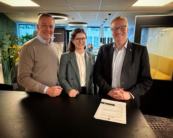 Et bilde av tre personer som står sammen ved et bord.