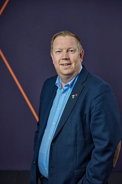 Mann i halvfigur som ser inn i kameraet.Brun bakgrunn.