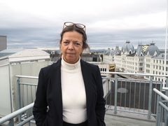 Kvinne i halvfigur som står på taketerrasse med bymiljø i bakgrunnen.