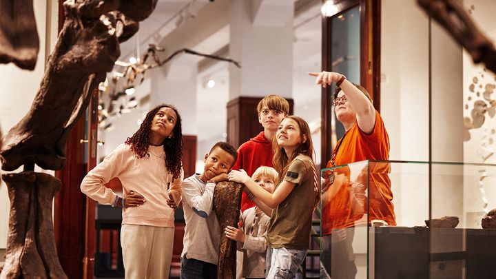 barn og omviser ser på dinosaurskjelett på museum