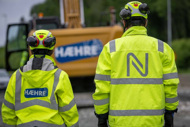 To%20personer%20i%20gule%20arbeidsjakker%20med%20logoene%20til%20H%E6hre%20og%20Nye%20Veier%2C%20foran%20en%20anleggsmaskin.