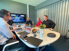 Personer som jobber sammen på møterom. Presentasjon på skjerm. Åpne laptoper. Smil og latter.
