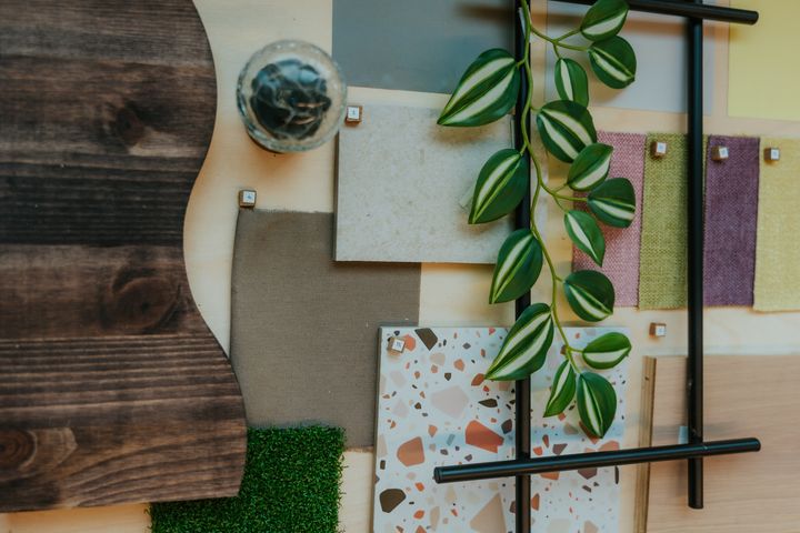 Prøver av forskjellige materialer og teksturer arrangert på et bord, inkludert tre, stoff, og kunstige planter.