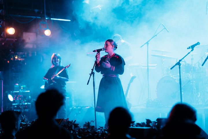 En sanger på scenen med band i bakgrunnen, omgitt av blått lys. Publikum foran.