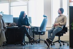 Bildet viser en mann og ei kvinne som sitter i et åpent kontorlandskap. De snakker sammen.