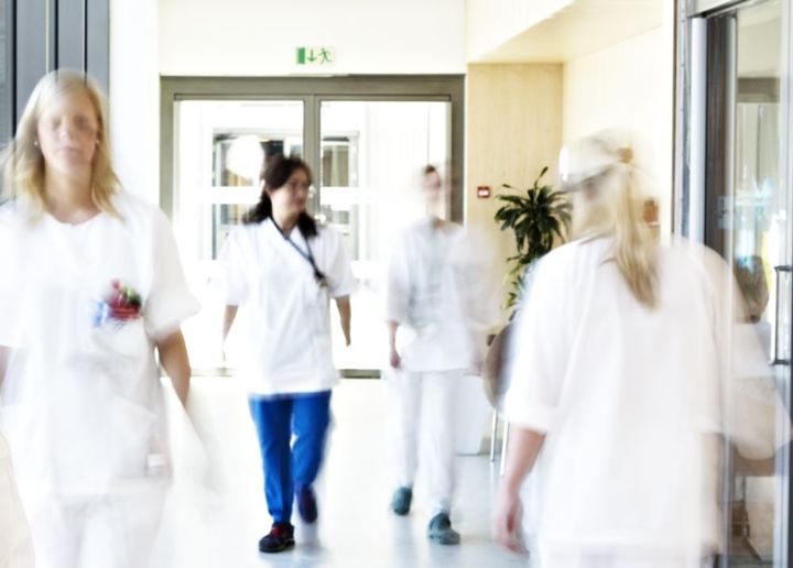 Bildet viser en sykehuskorridor og flere hvitkledde ansatte som går gjennom den.