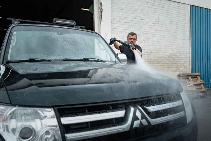 Bildet viser en mann som vasker en bil med en høyttrykksspyler.