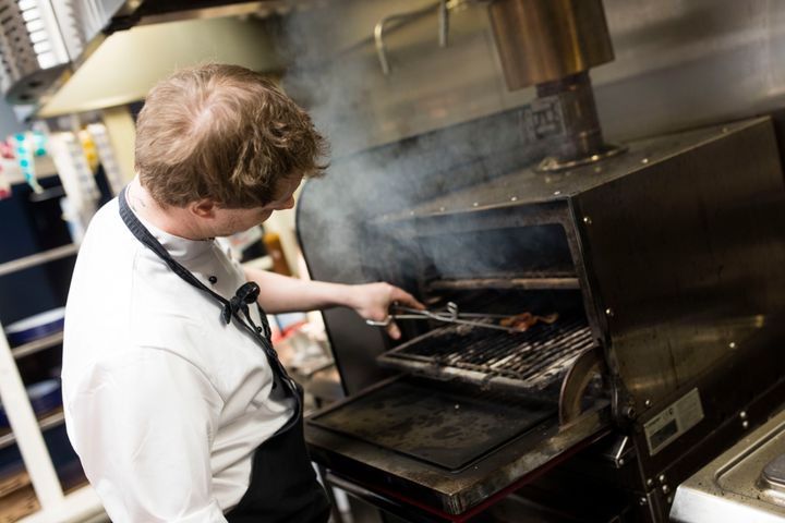 Bildet viser en kokk som tilbereder mat på et kjøkken.