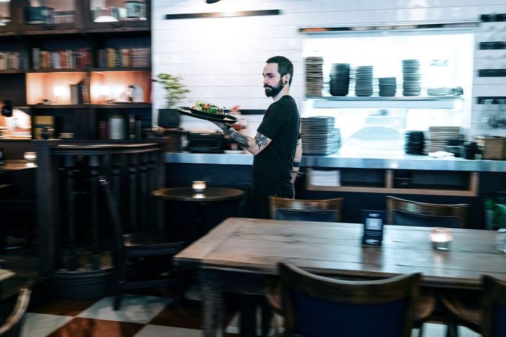 Bildet viser en servitør som bærer mat inne i en restaurant.