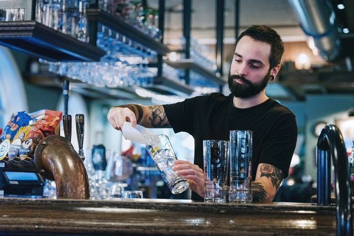 Bildet viser en mann som jobber i en bar. Han tømmer isbiter i et glass.