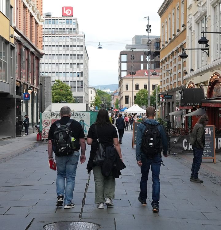 TO menn og en kvinne fotografert bakfra mens de går i en gate omringet av bygninger