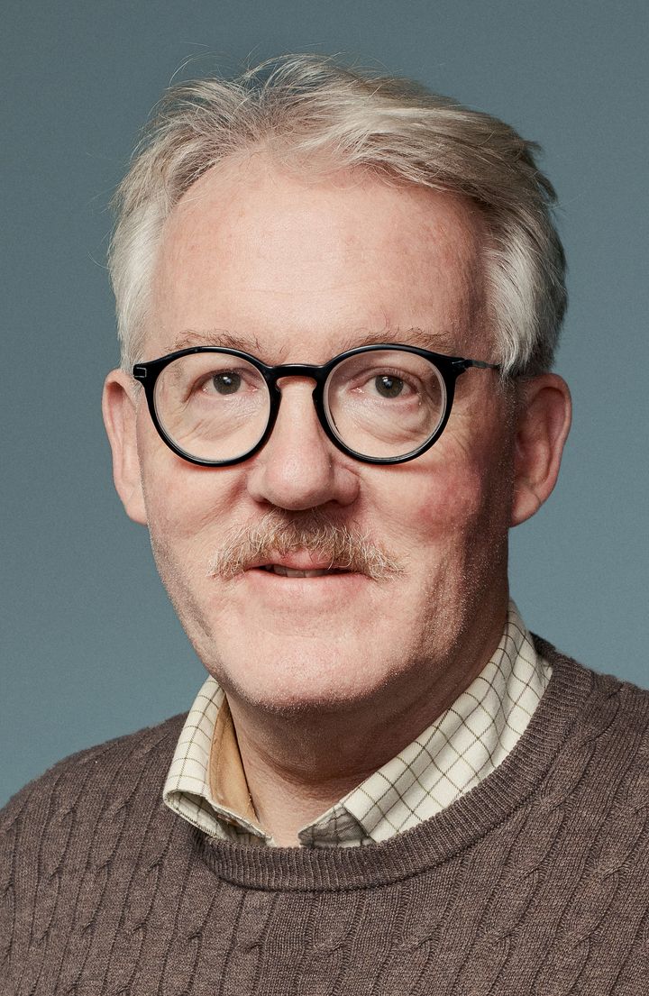 Mann med hvitt hår og sorte runde briller, ser inn i kamera.