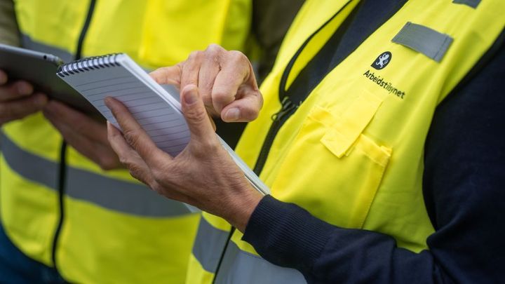 Bildet viser hendene til to inspektører som har på seg gul Arbeidstilsynet-vest.