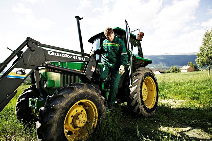 Mann  i grønn kjeledress på vei ut av traktor på et jorde