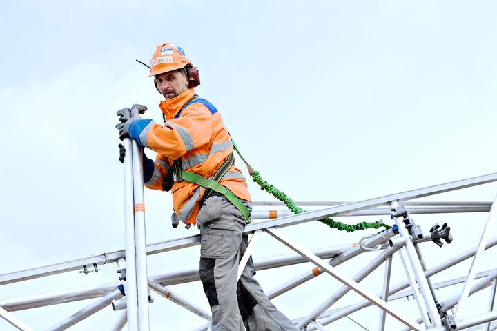 Arbeidstaker med verneutstyr monterer stillas i høyden.
