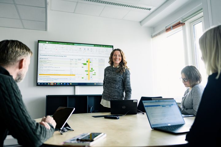 BIldet viser ei dame som snakker foran kolleger på jobb.