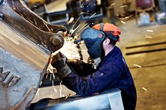 En sveiser i arbeidsklær og maske sveiser inne i en industrihall