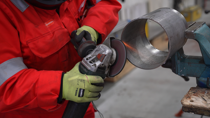 En sveiser i arbeidsklær sveiser på et rør