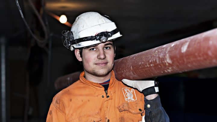 Ung arbeidstaker som løfter et rør på ryggen.
