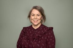 Kvinne  med vinrød bluse smiler mens hun ser i kamera.