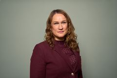 Kvinne med krøllete, brunt hår og rødbrun bluse, ser inn i kamera.