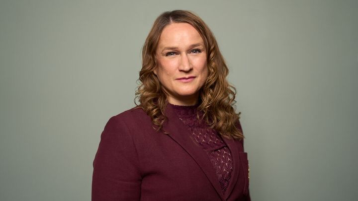 Kvinne med krøllet, mørkblondt hår ser inn i kamera