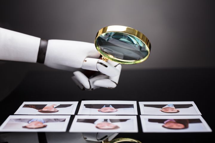 Robothånd holder forstørrelsesglass over bilder av mennesker.