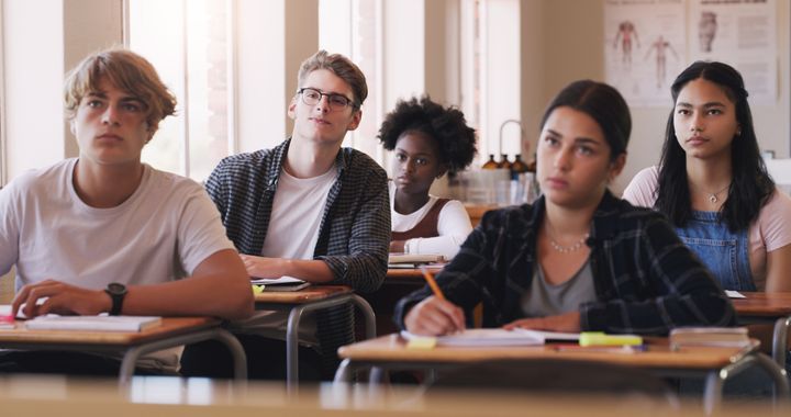 Foto av fem elever som sitter ved pultene sine i et klasserom