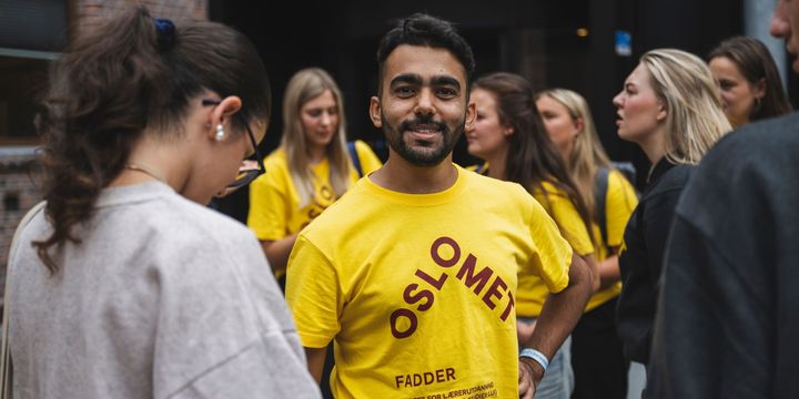 Ung mann i OsloMet-tskjorte ser rett i kamera. I bakgrunnen står flere studenter.