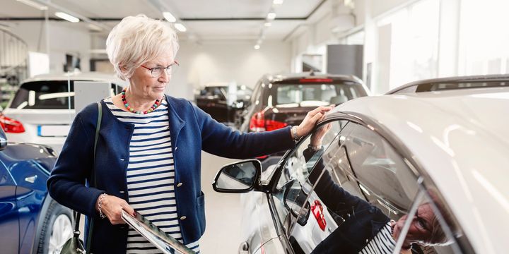 Eldre kvinne ser på en bil.