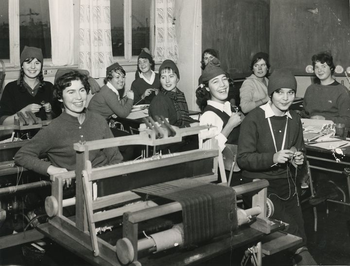 Studenter ved Den kvinnelige industriskole sitter ved pultene sine og jobber. Alle har på seg nisseluser.