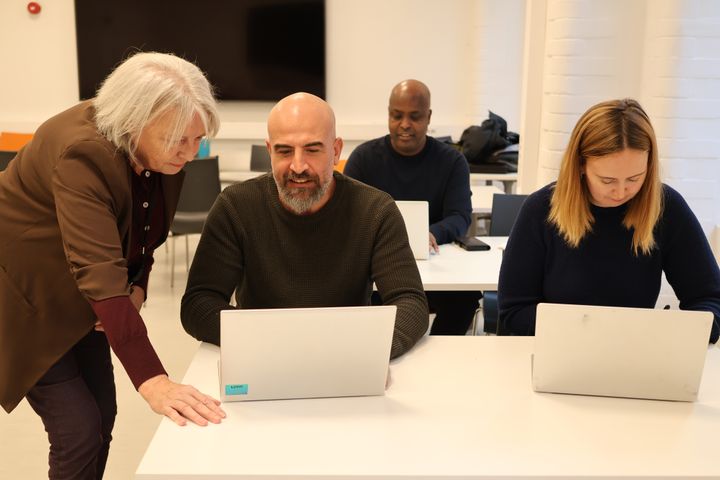 Foto av en lærer og tre voksne elever som ser på data i et klasserom
