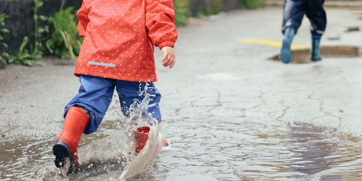Barn leker i regntøy og hopper i en vannpytt.